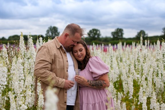 Couple standing closely together in a flower field, with white blooms around them.