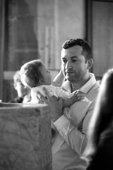 A man holding a baby while interacting in a busy, softly lit church in front of a stone font.