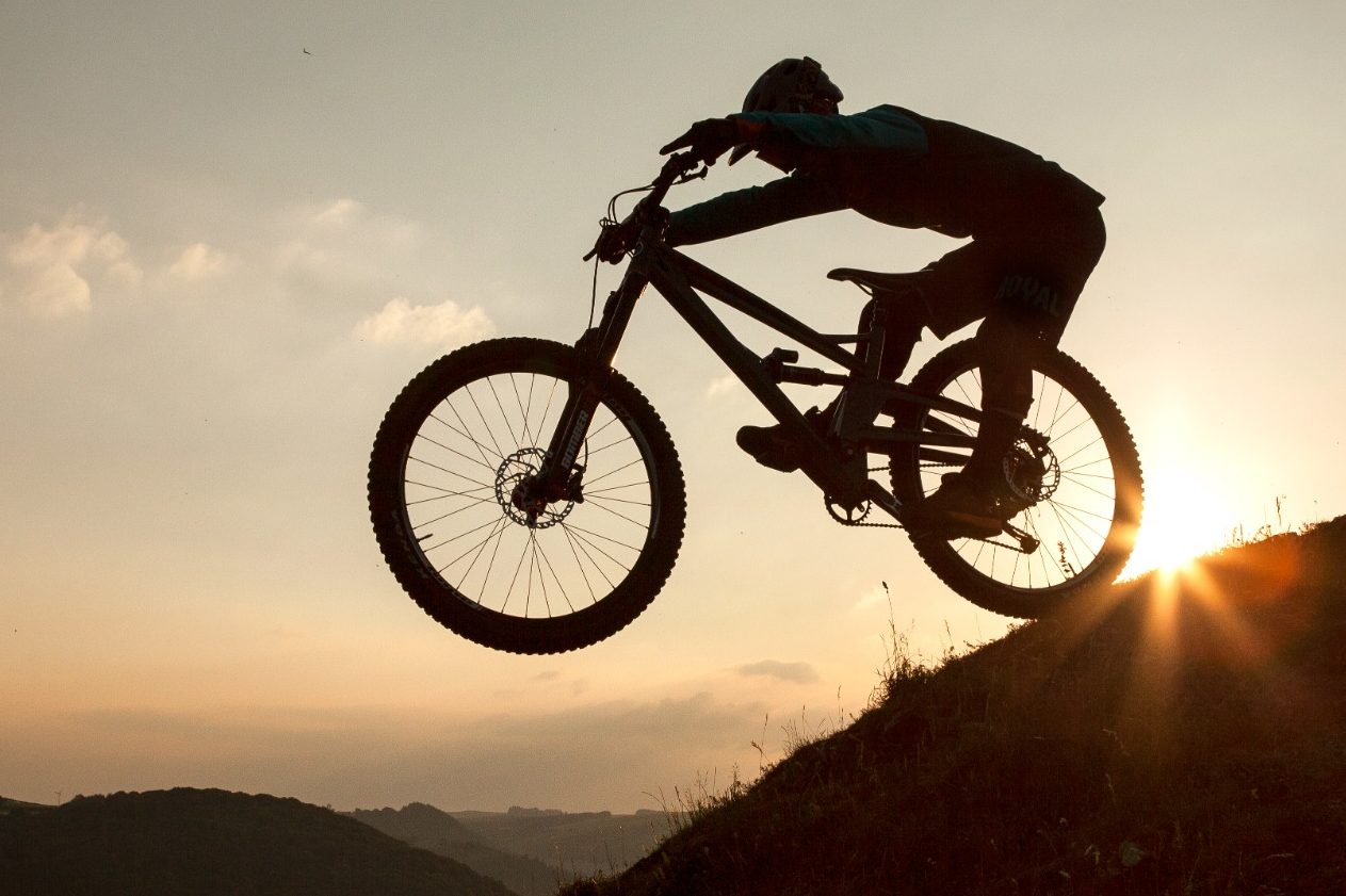 Silhouette of a cyclist performing a jump against a sunset backdrop.