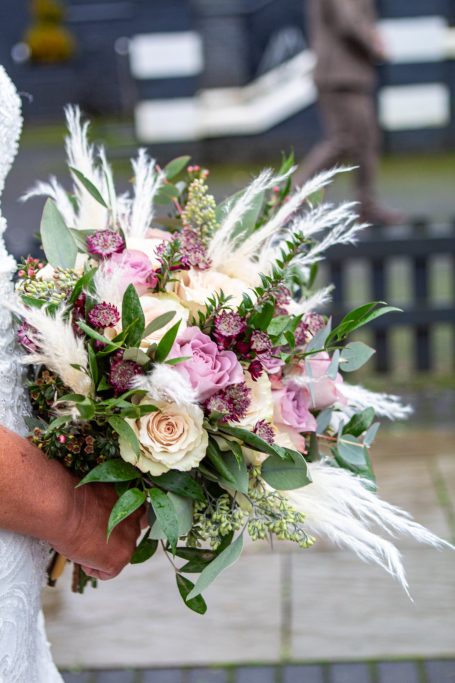 A hand holding a wedding bouquet with pink and white flowers and greenery.