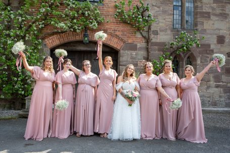 A bride in a white dress with bridesmaids in pink dresses, all holding flowers.