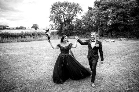 A couple joyfully walks hand in hand, dressed elegantly for their wedding day.