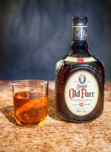 A bottle of Old Parr whisky next to a glass filled with whisky and an orange slice.