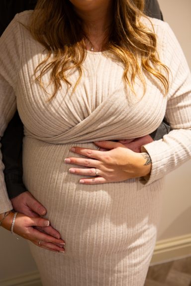 A pregnant woman in a fitted dress with a hand resting on her belly.