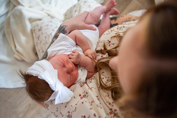 A mother cradles a newborn baby wearing a white outfit and a bow headband.