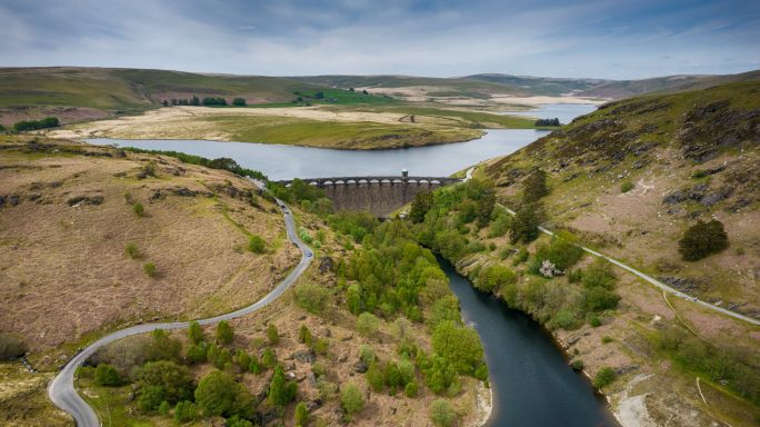 A scenic view of a winding river surrounded by hills and greenery under a blue sky.