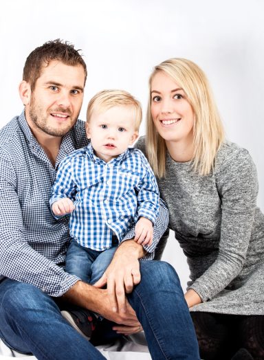 A smiling family consisting of a man, woman, and a toddler sitting together.