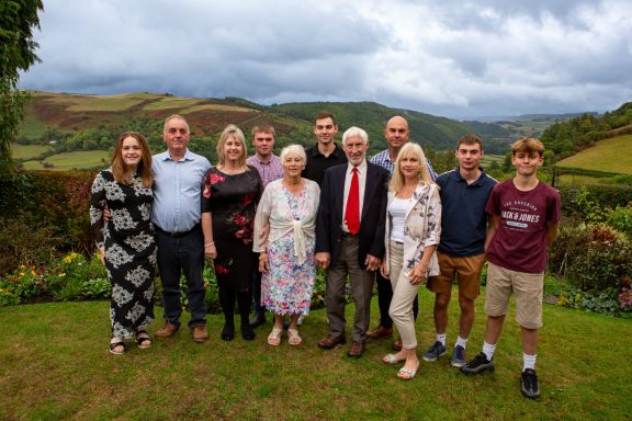 A family of twelve people posing together outdoors with a mountainous backdrop.