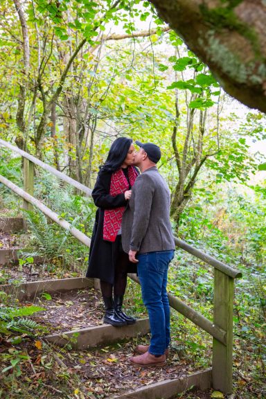 A couple sharing a kiss on wooden stairs surrounded by greenery.