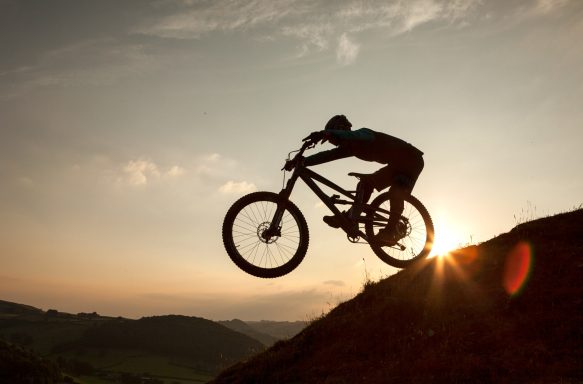 Silhouette of a cyclist jumping off a hill against a sunset backdrop.