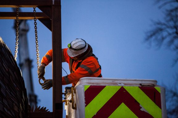 A construction worker in high-visibility gear adjusts equipment from a lift.