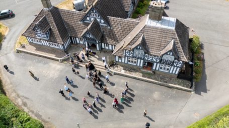 Aerial view of a group of people gathered outside a black and white timber-framed building.