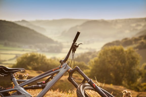 Mountain bikes resting on a hilltop with a scenic valley and hills in the background.